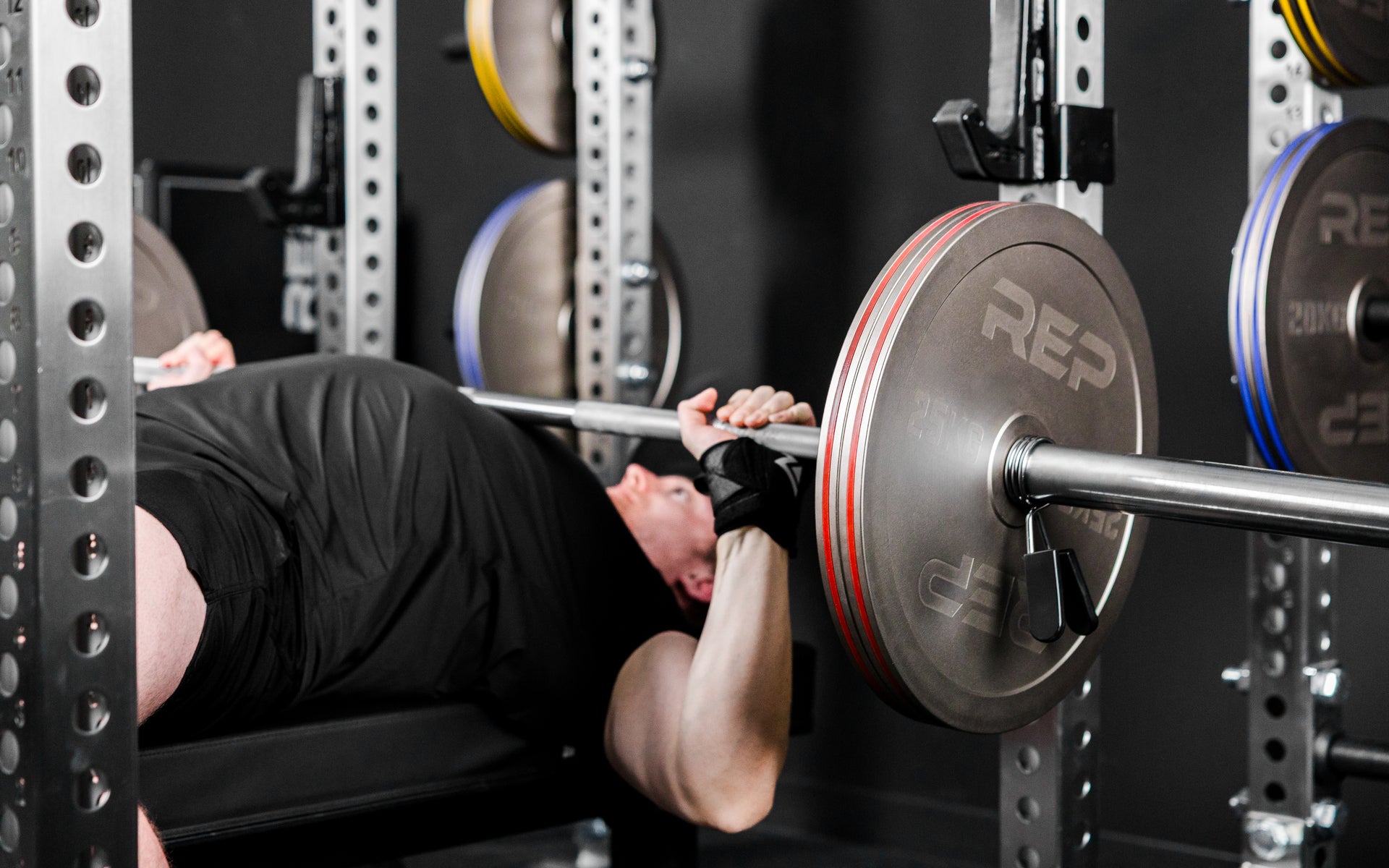 An athlete bench pressing in a PR-5000 rack with Rep Fitness Calibrated Steel Plates (KG) loaded on the barbell
