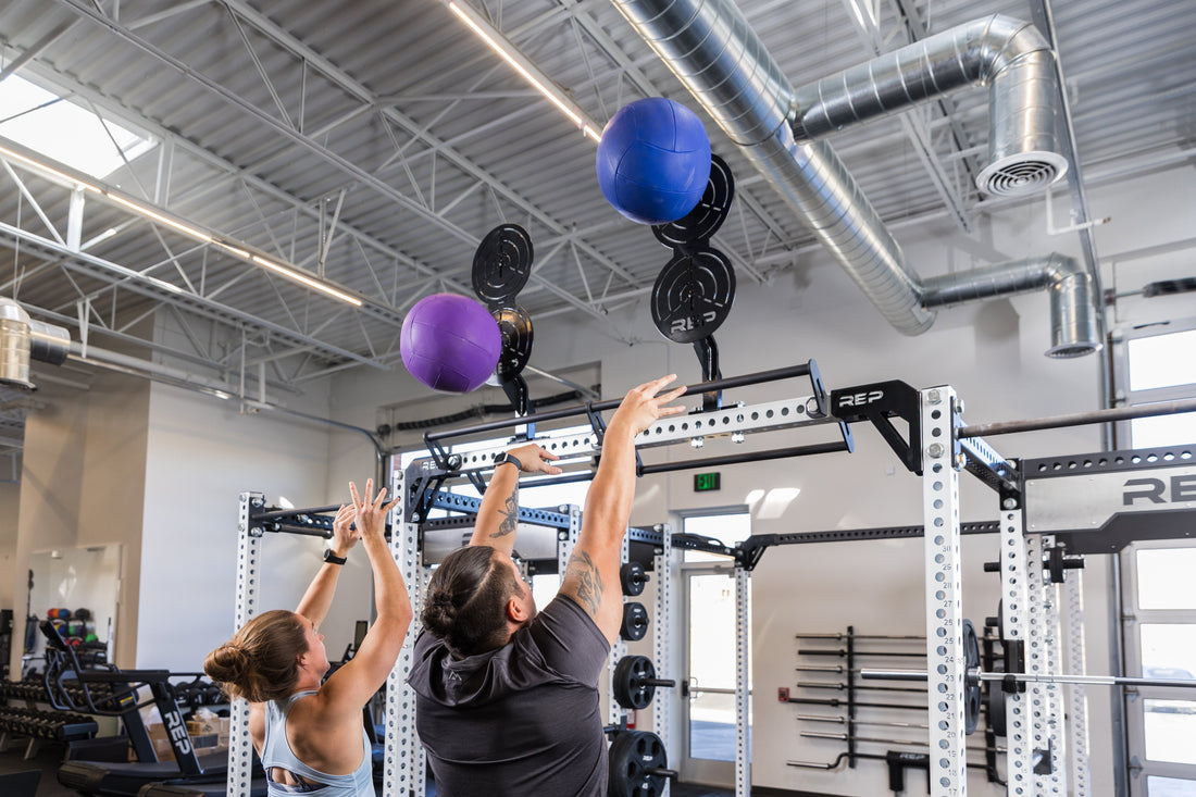 Athletes throw medicine balls at a wall ball target.